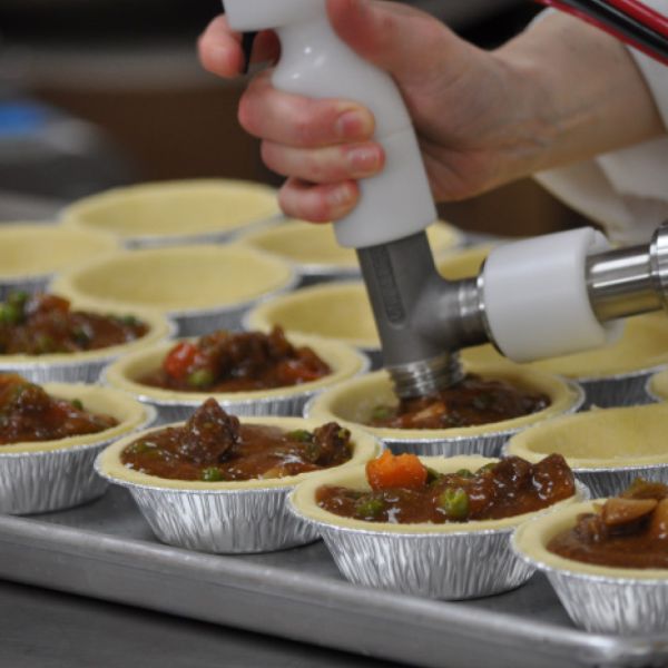 Handdosierer befüllt Pastetchen mit herzhafter Fleisch-Gemüse-Füllung